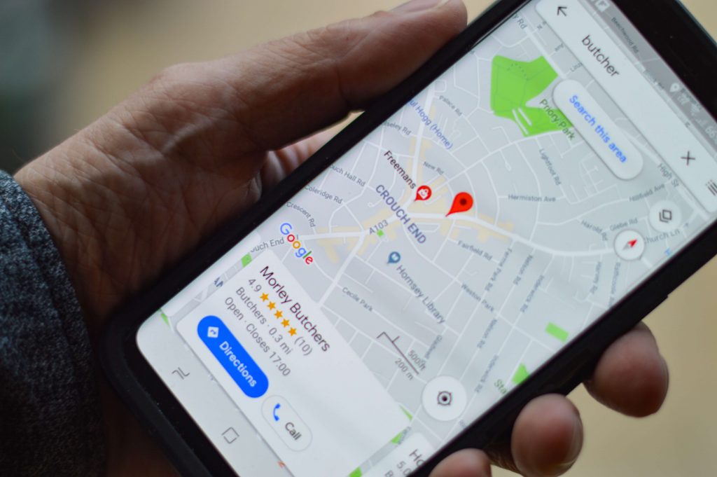 Image of a mobile phone in a mans hand showing a Google map after a search for 'butcher'.